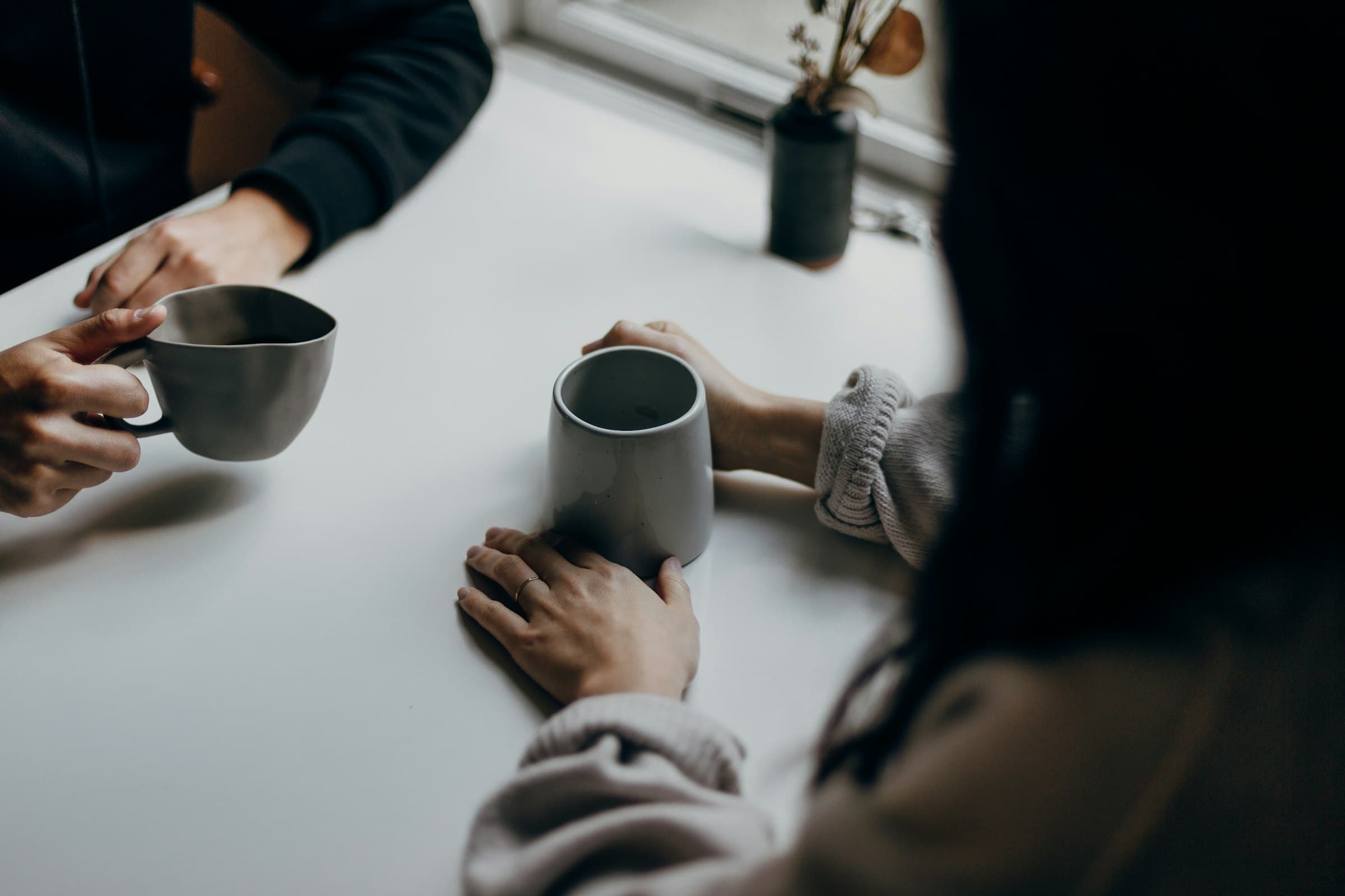 Zwei Menschen mit Kaffeetassen im Gespräch am Tisch